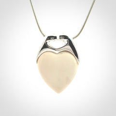This picture shows a pendant that we have carved in a combination of sterling silver and woolly mammoth. It shows a symbolic kiss, with two heads coming together and both embracing a woolly mammoth heart. The necklace is a sterling silver chain.