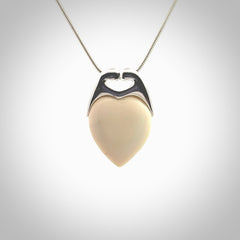 This picture shows a pendant that we have carved in a combination of sterling silver and woolly mammoth. It shows a symbolic kiss, with two heads coming together and both embracing a woolly mammoth heart. The necklace is a sterling silver chain.