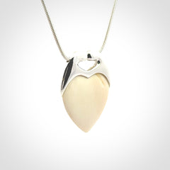This picture shows a pendant that we have carved in a combination of sterling silver and woolly mammoth. It shows a symbolic kiss, with two heads coming together and both embracing a woolly mammoth heart. The necklace is a sterling silver chain.