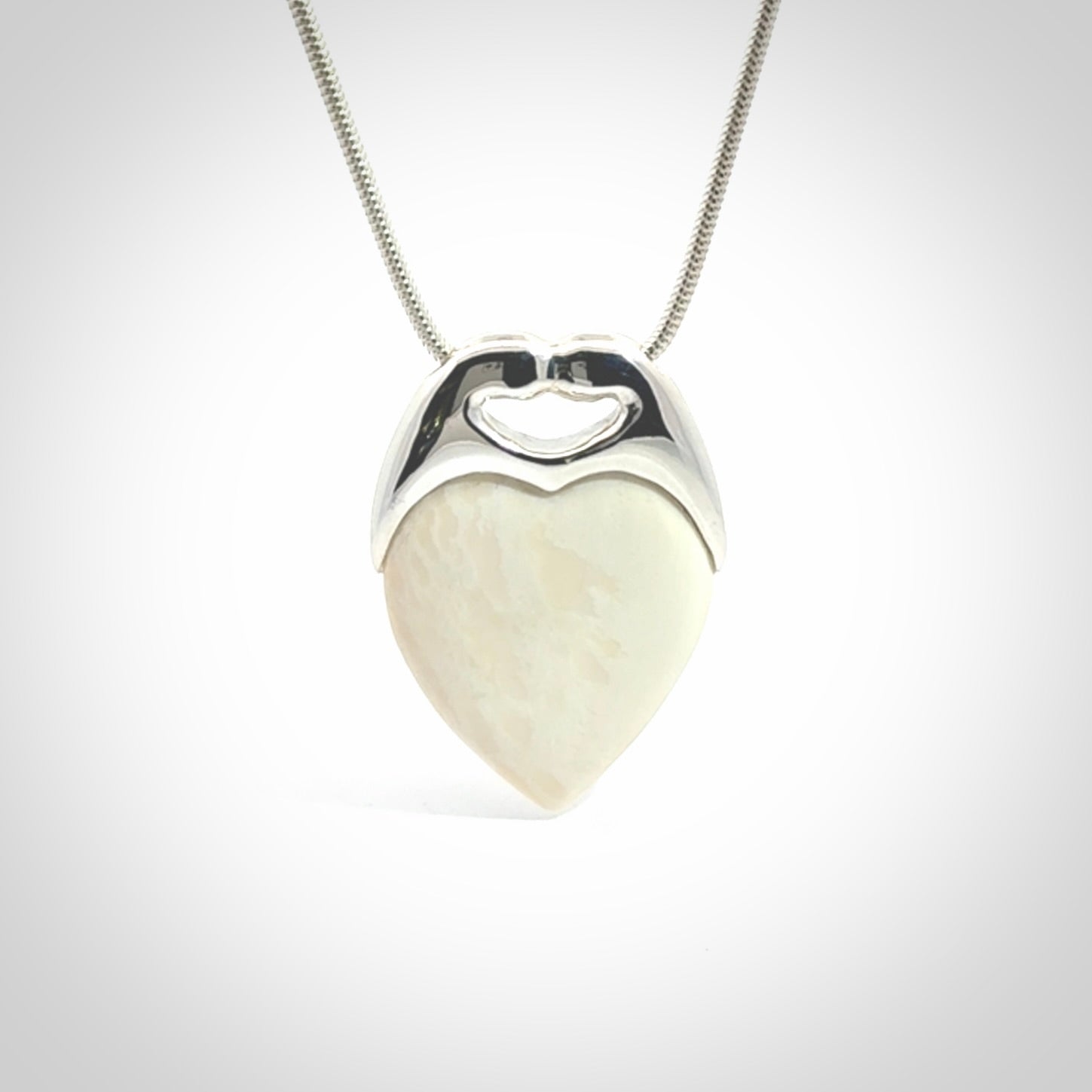 This picture shows a pendant that we have carved in a combination of sterling silver and woolly mammoth. It shows a symbolic kiss, with two heads coming together and both embracing a woolly mammoth heart. The necklace is a sterling silver chain.