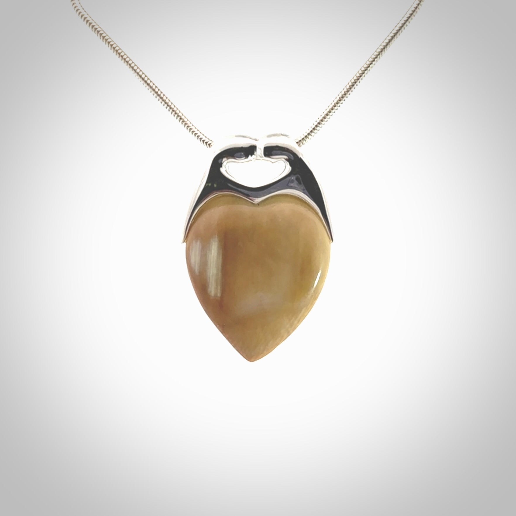 This picture shows a pendant that we have carved in a combination of sterling silver and woolly mammoth. It shows a symbolic kiss, with two heads coming together and both embracing a woolly mammoth heart. The necklace is a sterling silver chain.