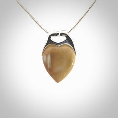 This picture shows a pendant that we have carved in a combination of sterling silver and woolly mammoth. It shows a symbolic kiss, with two heads coming together and both embracing a woolly mammoth heart. The necklace is a sterling silver chain.