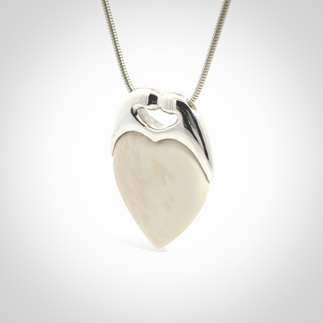 This picture shows a pendant that we have carved in a combination of sterling silver and woolly mammoth. It shows a symbolic kiss, with two heads coming together and both embracing a woolly mammoth heart. The necklace is a sterling silver chain.