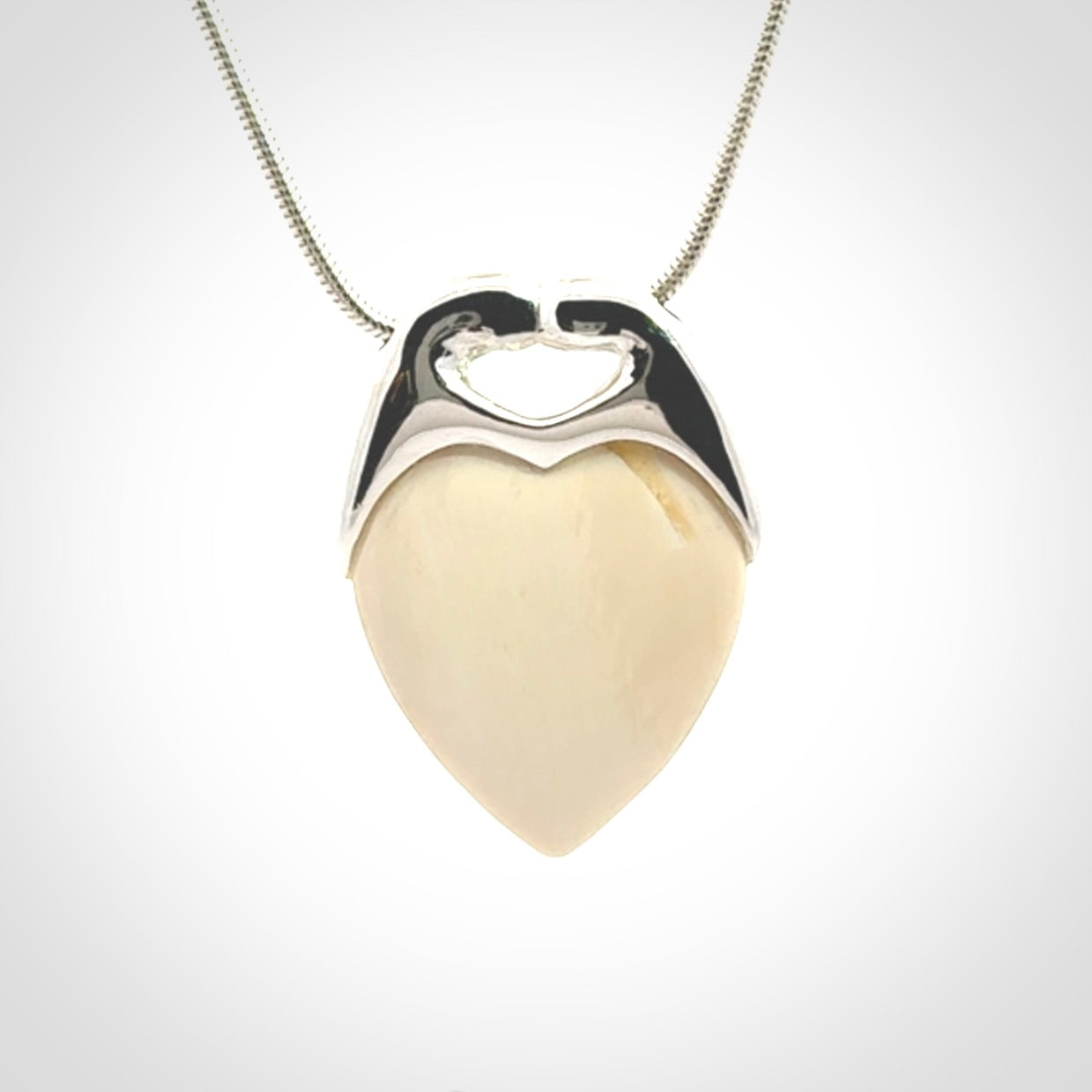 This picture shows a pendant that we have carved in a combination of sterling silver and woolly mammoth. It shows a symbolic kiss, with two heads coming together and both embracing a woolly mammoth heart. The necklace is a sterling silver chain.