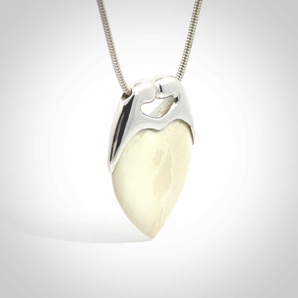 This picture shows a pendant that we have carved in a combination of sterling silver and woolly mammoth. It shows a symbolic kiss, with two heads coming together and both embracing a woolly mammoth heart. The necklace is a sterling silver chain.