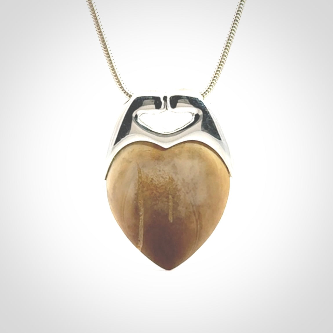 This picture shows a pendant that we have carved in a combination of sterling silver and woolly mammoth. It shows a symbolic kiss, with two heads coming together and both embracing a woolly mammoth heart. The necklace is a sterling silver chain.