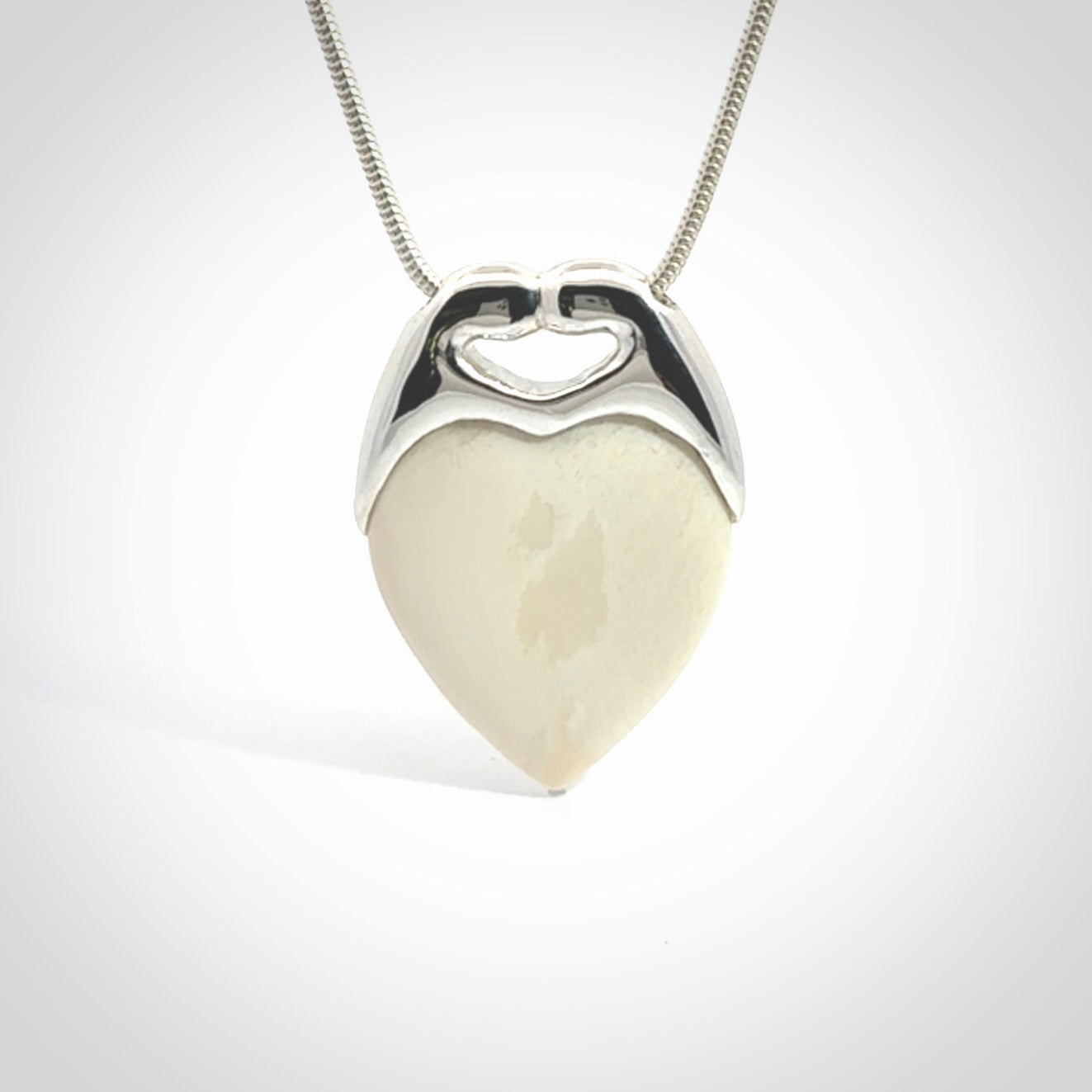 This picture shows a pendant that we have carved in a combination of sterling silver and woolly mammoth. It shows a symbolic kiss, with two heads coming together and both embracing a woolly mammoth heart. The necklace is a sterling silver chain.