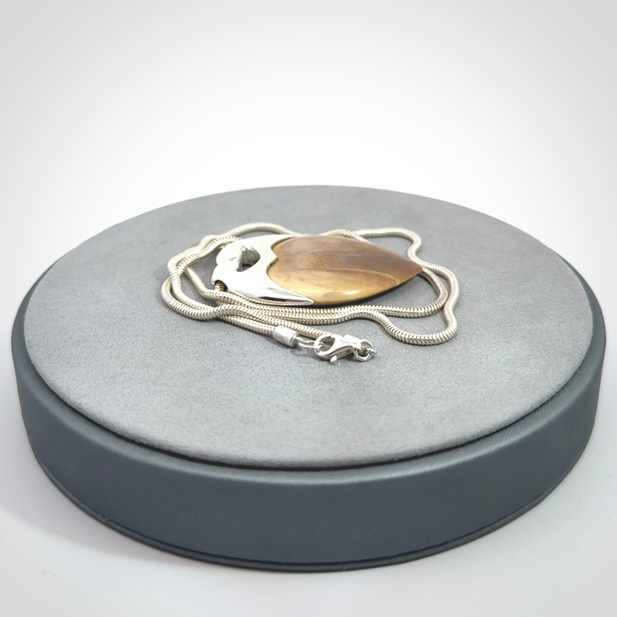 This picture shows a pendant that we have carved in a combination of sterling silver and woolly mammoth. It shows a symbolic kiss, with two heads coming together and both embracing a woolly mammoth heart. The necklace is a sterling silver chain.