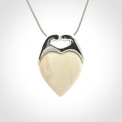 This picture shows a pendant that we have carved in a combination of sterling silver and woolly mammoth. It shows a symbolic kiss, with two heads coming together and both embracing a woolly mammoth heart. The necklace is a sterling silver chain.