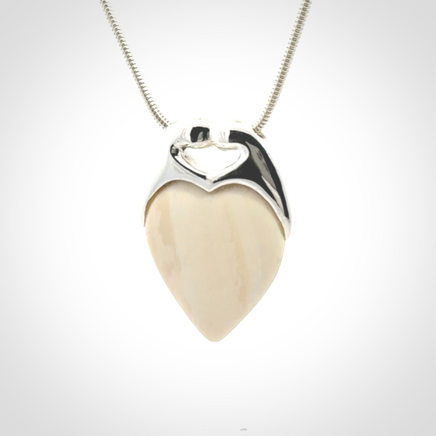 This picture shows a pendant that we have carved in a combination of sterling silver and woolly mammoth. It shows a symbolic kiss, with two heads coming together and both embracing a woolly mammoth heart. The necklace is a sterling silver chain.
