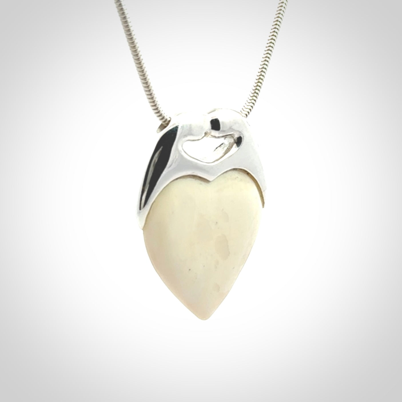 This picture shows a pendant that we have carved in a combination of sterling silver and woolly mammoth. It shows a symbolic kiss, with two heads coming together and both embracing a woolly mammoth heart. The necklace is a sterling silver chain.