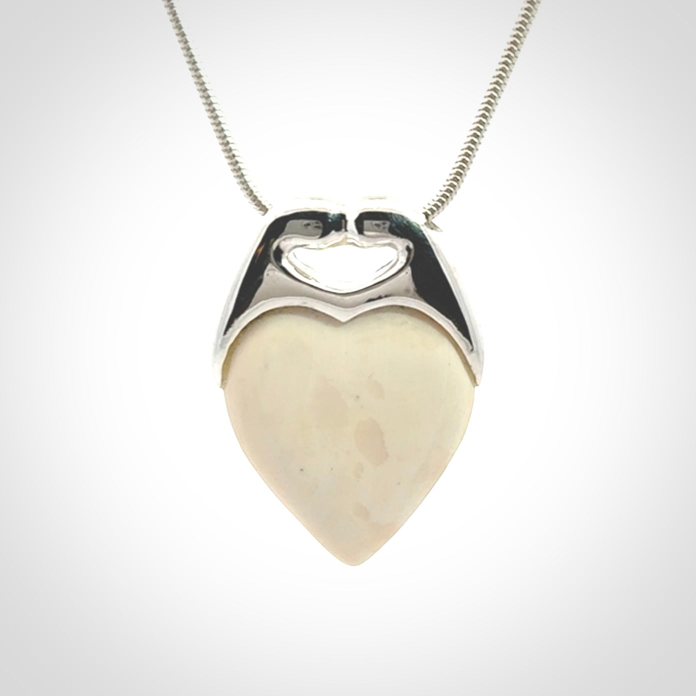 This picture shows a pendant that we have carved in a combination of sterling silver and woolly mammoth. It shows a symbolic kiss, with two heads coming together and both embracing a woolly mammoth heart. The necklace is a sterling silver chain.
