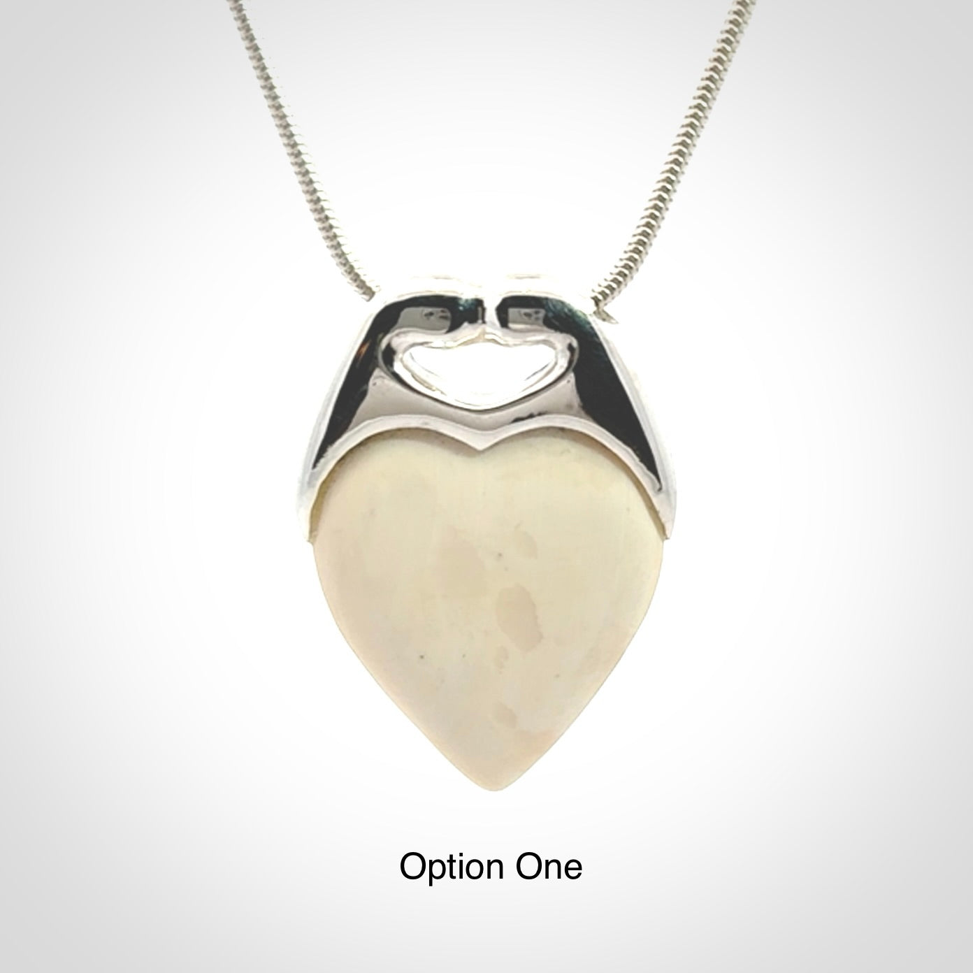 This picture shows a pendant that we have carved in a combination of sterling silver and woolly mammoth. It shows a symbolic kiss, with two heads coming together and both embracing a woolly mammoth heart. The necklace is a sterling silver chain.