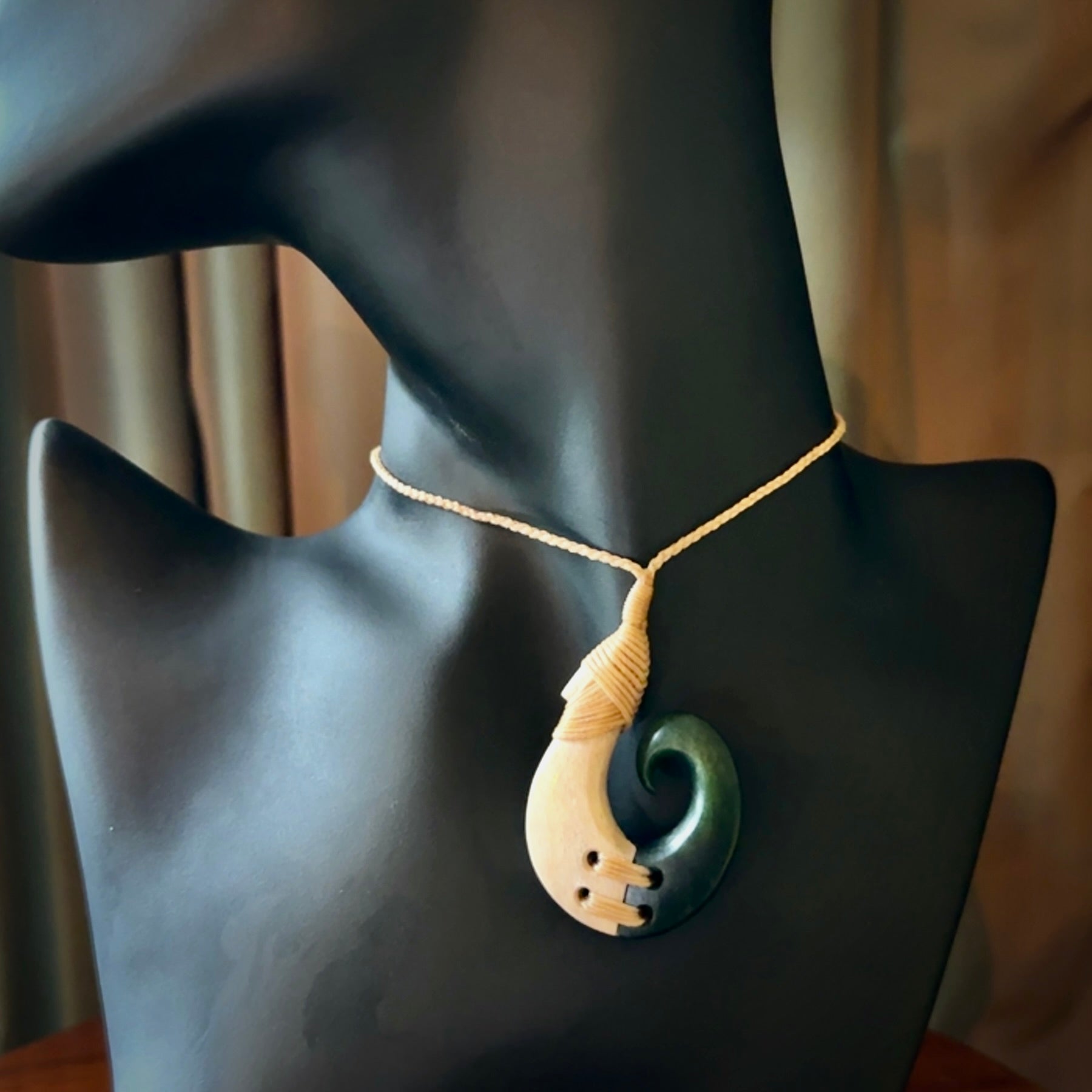 This photo shows a wonderful hand carved New Zealand jade and Whale Bone hook pendant. The hook is suspended on a beige four plait cord that is length adjustable.