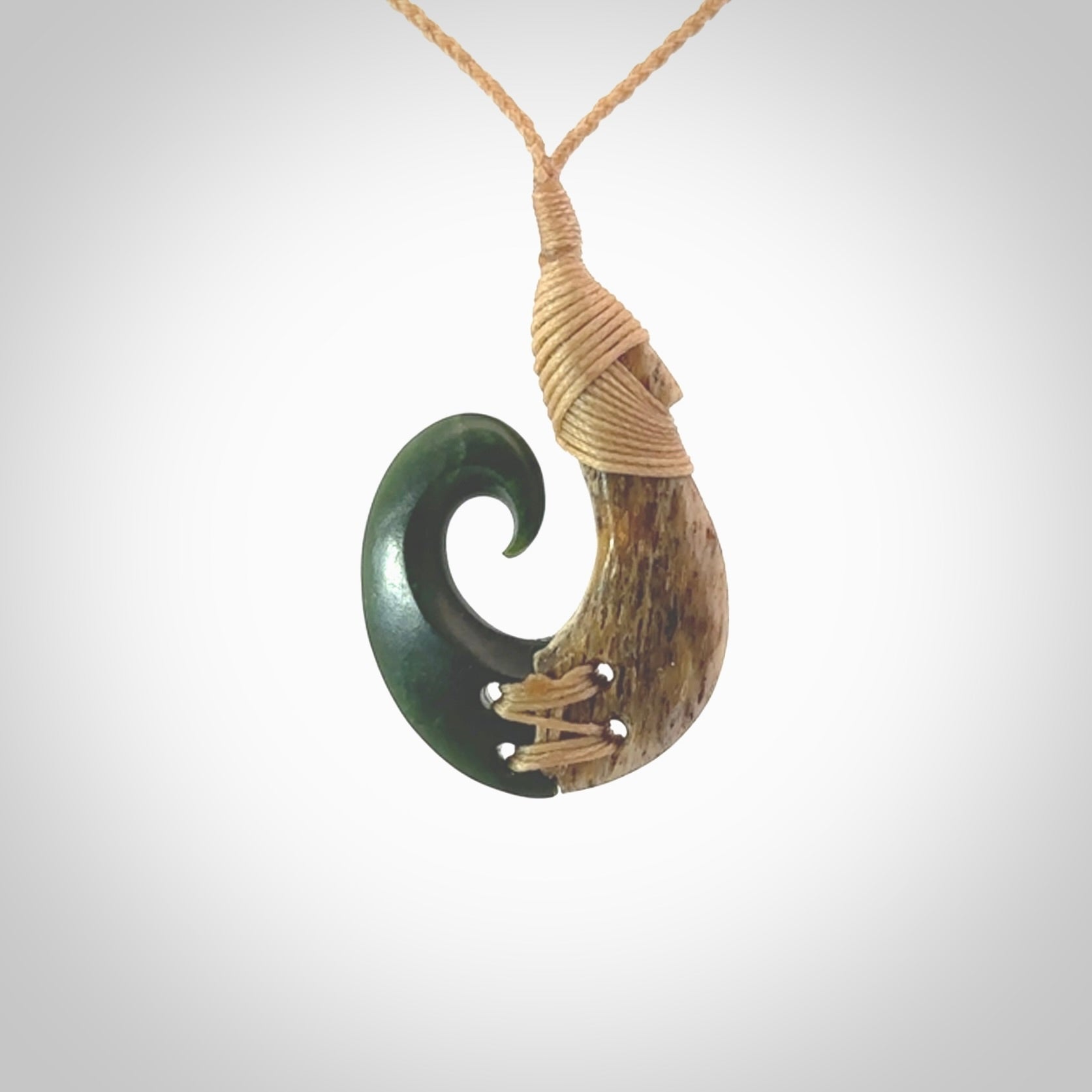 This photo shows a wonderful hand carved New Zealand jade and Whale Bone hook pendant. The hook is suspended on a beige four plait cord that is length adjustable.