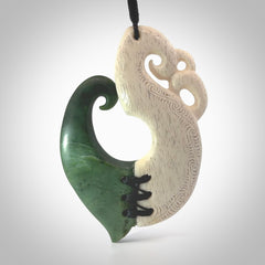 This photo shows a wonderful hand carved New Zealand jade and Whale Bone Manaia with hook pendant. The hook is suspended on a black four plait cord that is length adjustable.
