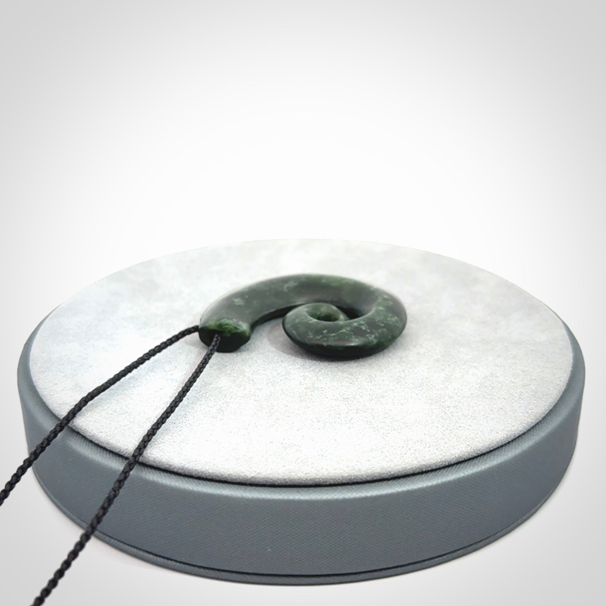 This picture shows a koru pendant, hand carved from New Zealand jade. We will provide this with an adjustable black plaited cord. This has been hand carved by Kyohei Noguchi. One only pendant, shipped to you with express courier.