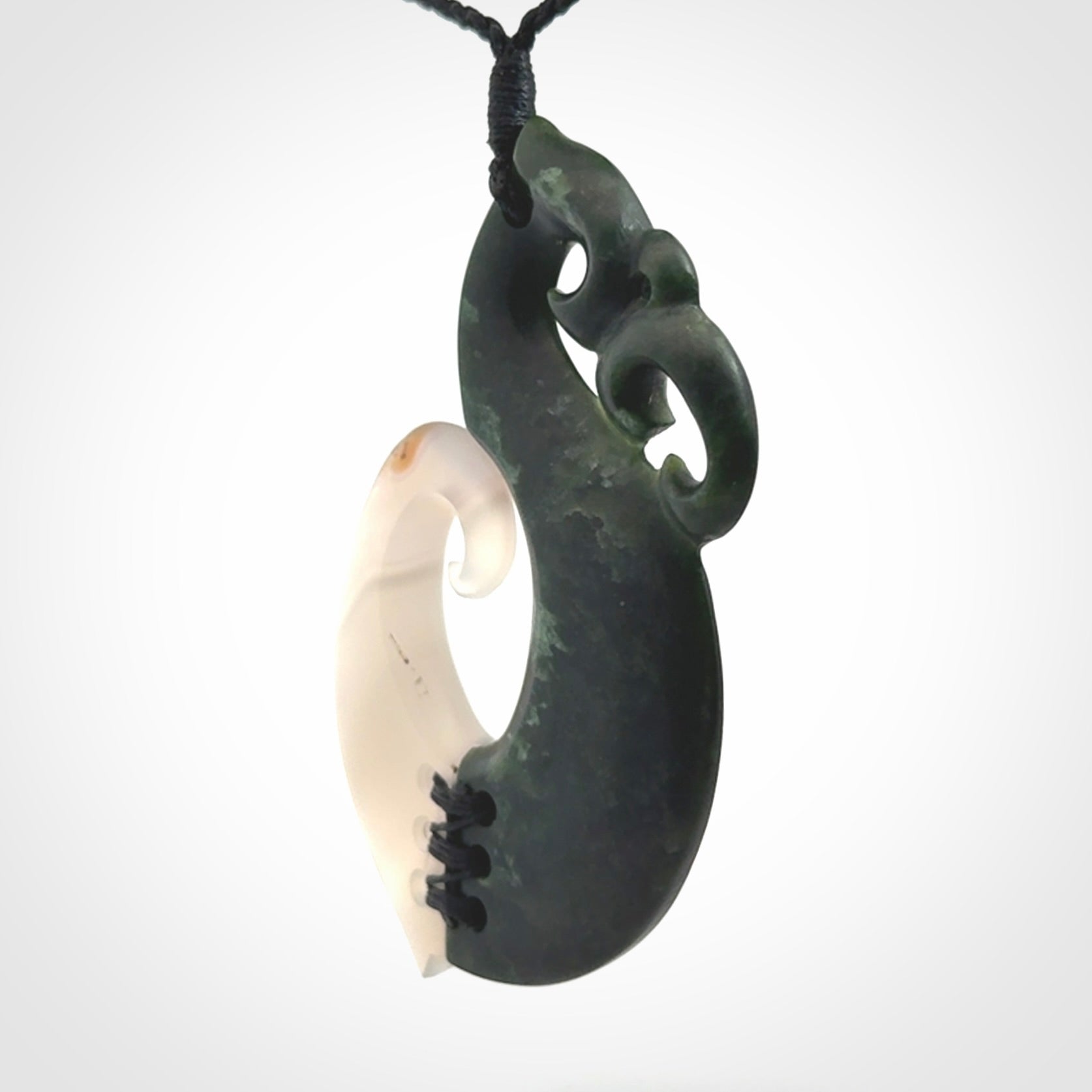 This photo shows a wonderful hand carved New Zealand jade and Japanese Agate Manaia with hook pendant. The hook is suspended on a black four plait cord that is length adjustable.