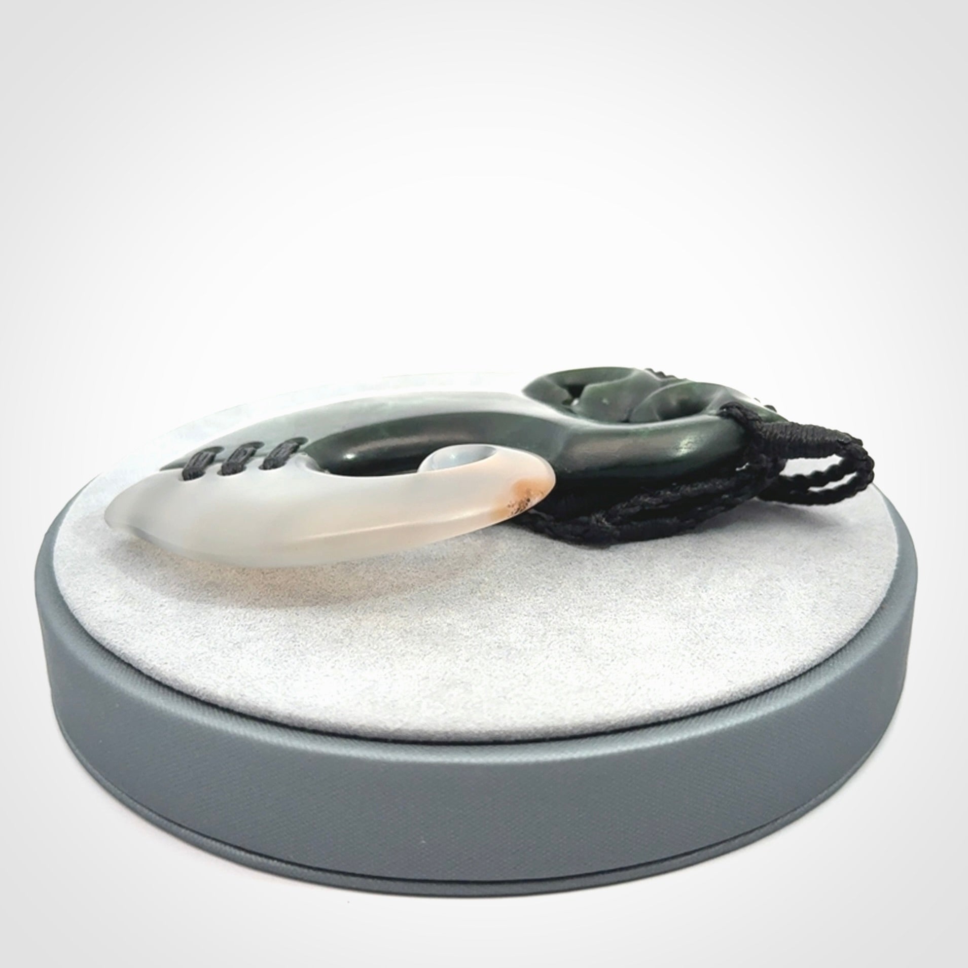 This photo shows a wonderful hand carved New Zealand jade and Japanese Agate Manaia with hook pendant. The hook is suspended on a black four plait cord that is length adjustable.
