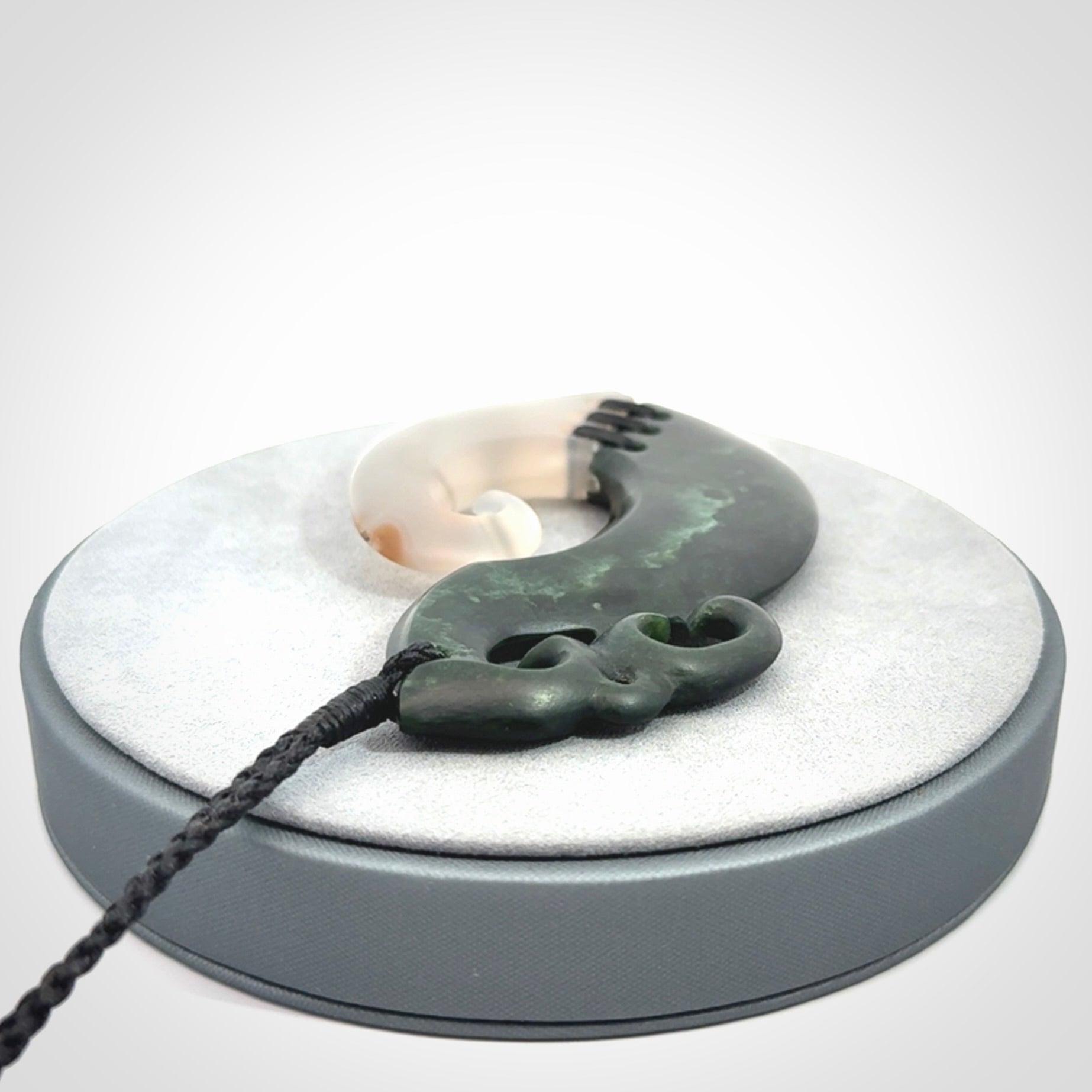 This photo shows a wonderful hand carved New Zealand jade and Japanese Agate Manaia with hook pendant. The hook is suspended on a black four plait cord that is length adjustable.