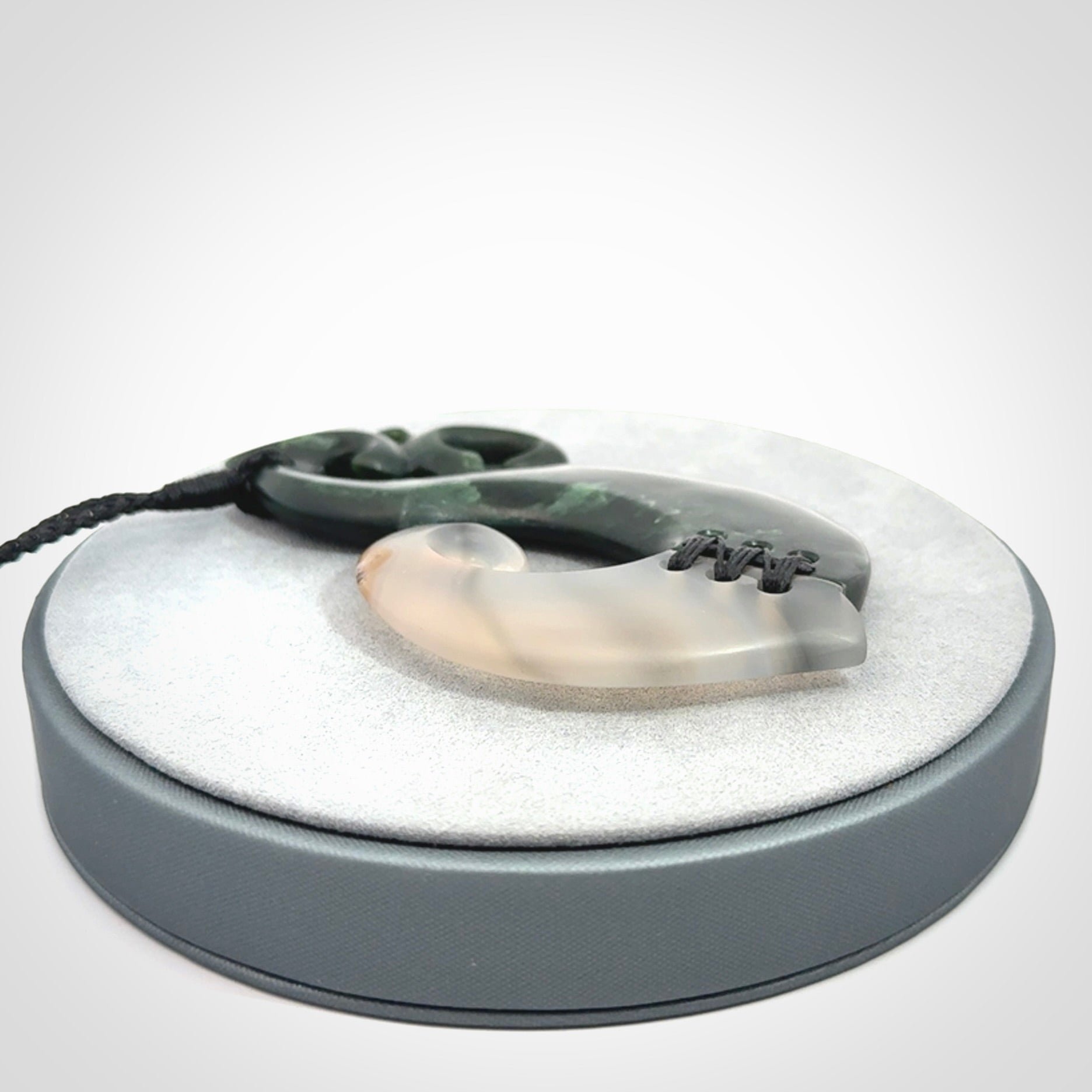 This photo shows a wonderful hand carved New Zealand jade and Japanese Agate Manaia with hook pendant. The hook is suspended on a black four plait cord that is length adjustable.