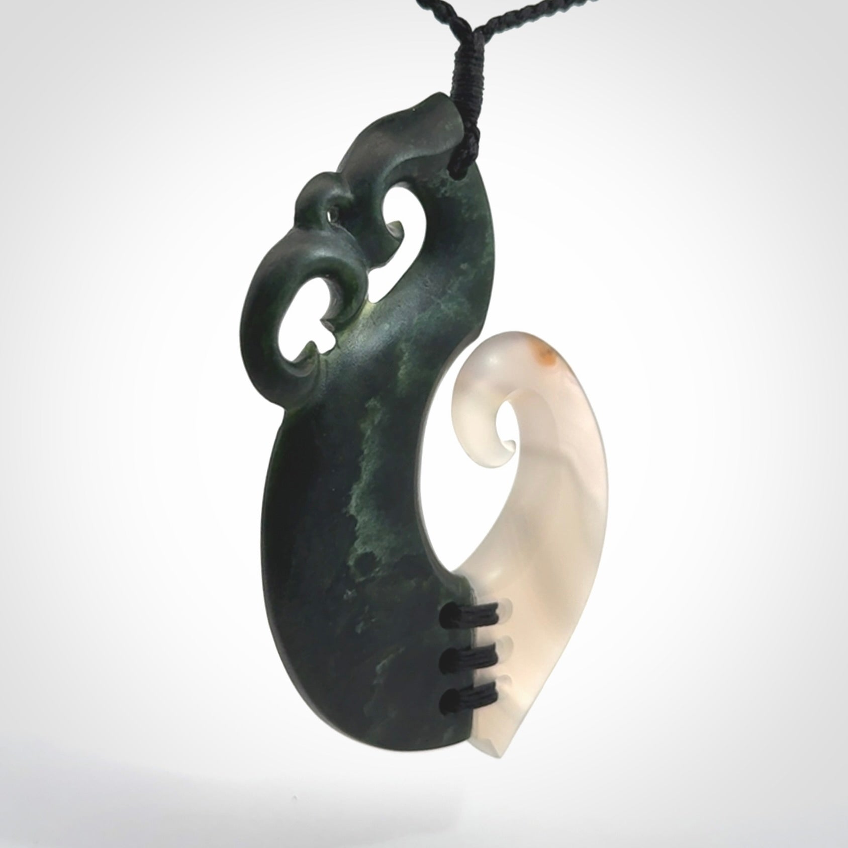 This photo shows a wonderful hand carved New Zealand jade and Japanese Agate Manaia with hook pendant. The hook is suspended on a black four plait cord that is length adjustable.