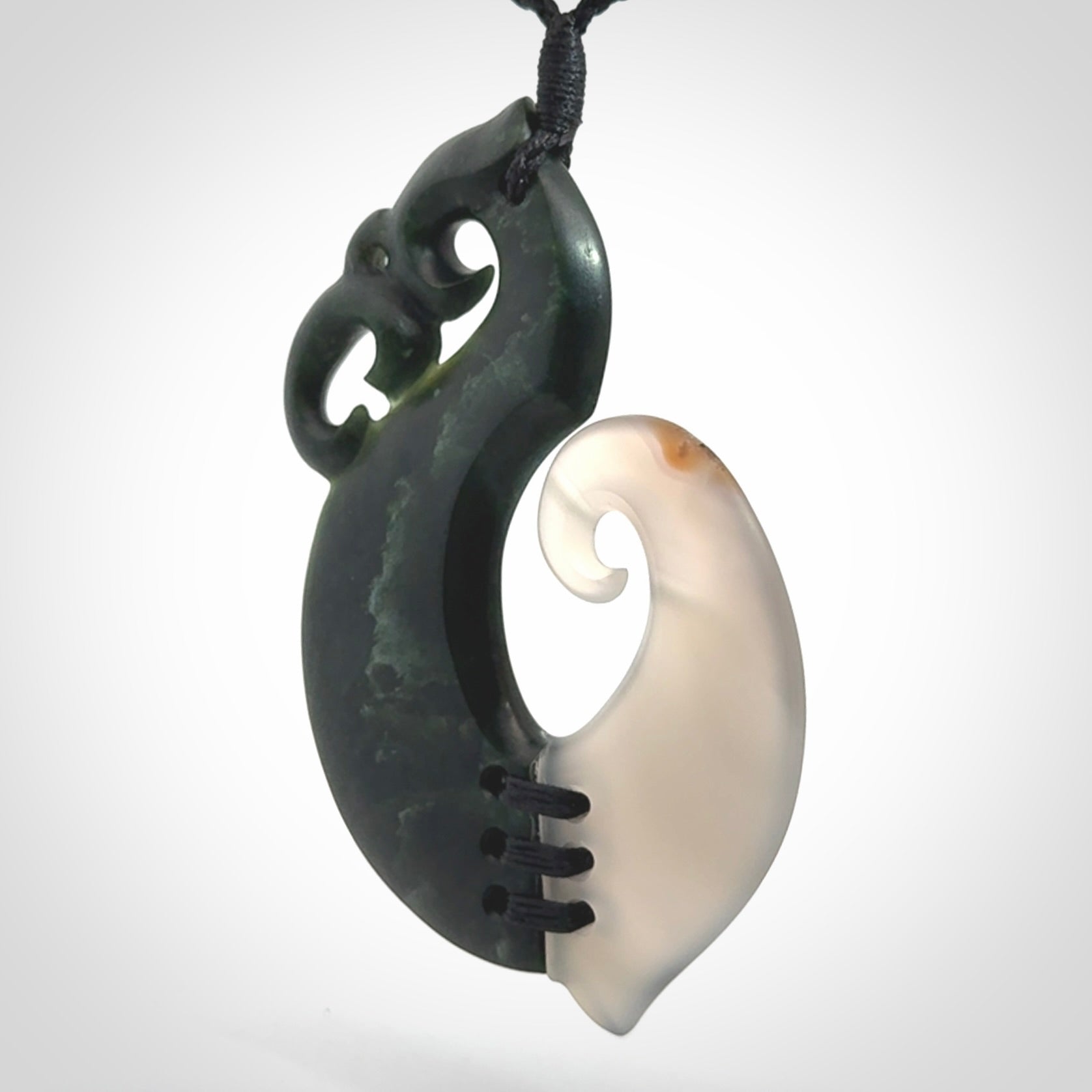 This photo shows a wonderful hand carved New Zealand jade and Japanese Agate Manaia with hook pendant. The hook is suspended on a black four plait cord that is length adjustable.