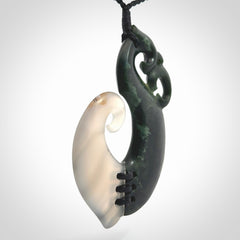 This photo shows a wonderful hand carved New Zealand jade and Japanese Agate Manaia with hook pendant. The hook is suspended on a black four plait cord that is length adjustable.