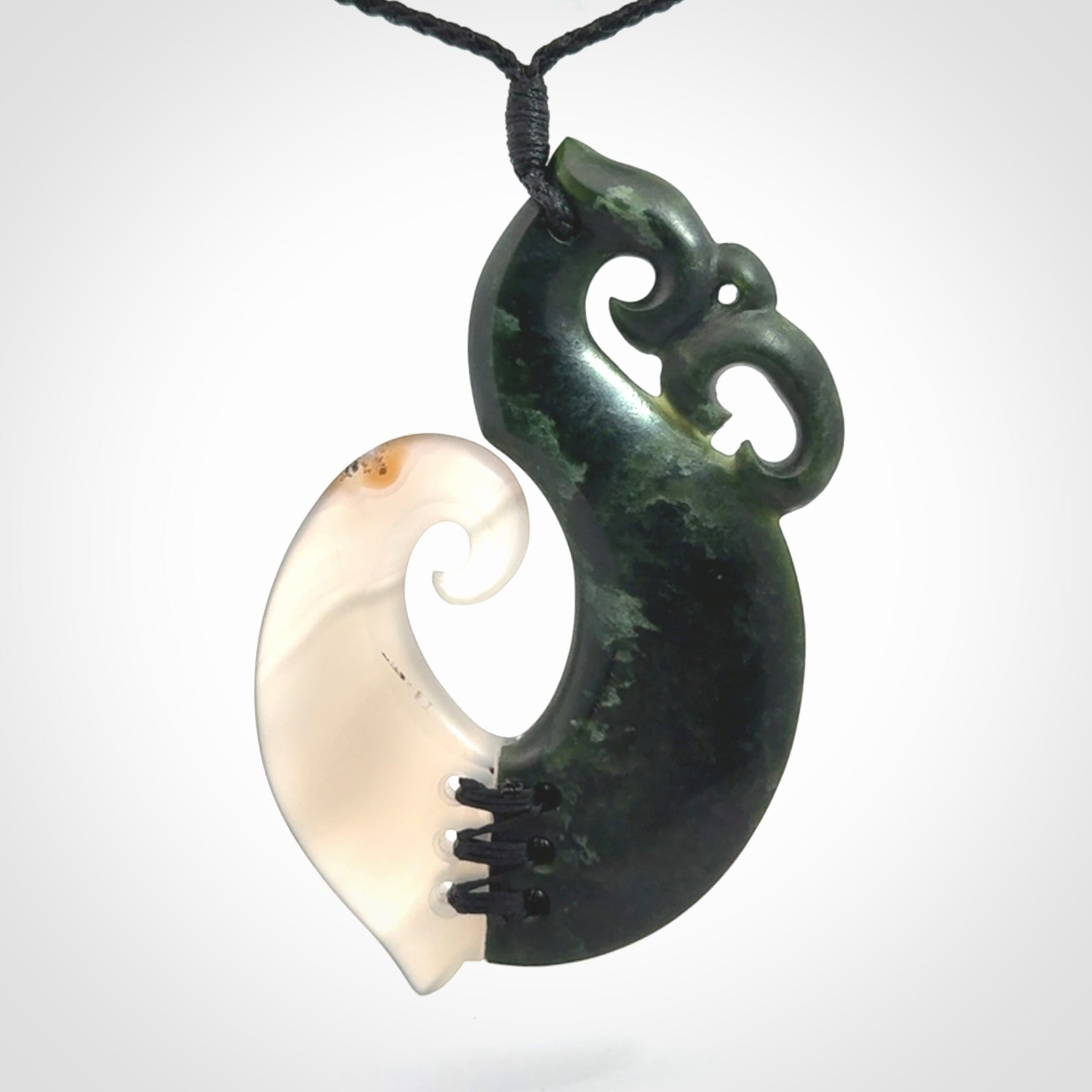 This photo shows a wonderful hand carved New Zealand jade and Japanese Agate Manaia with hook pendant. The hook is suspended on a black four plait cord that is length adjustable.