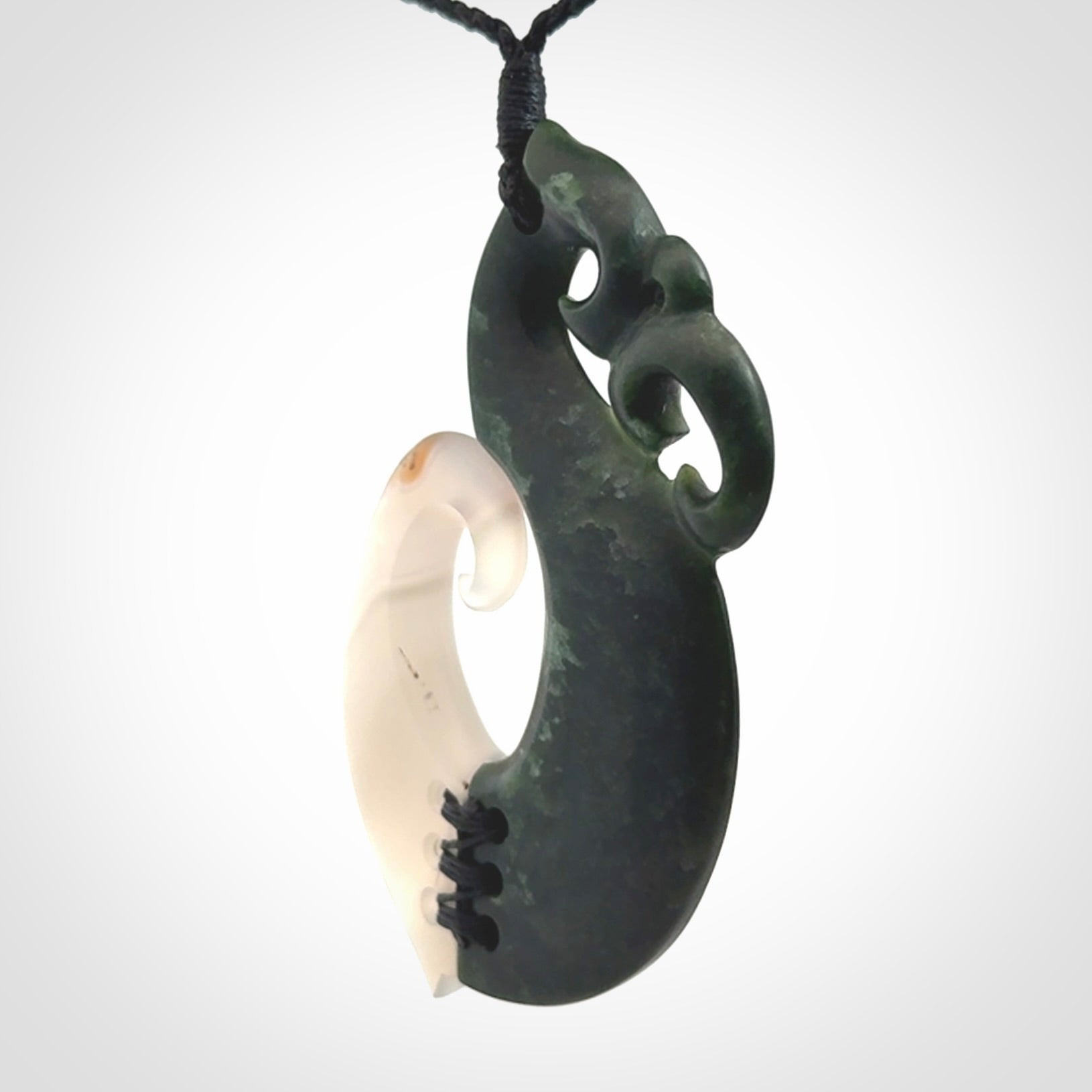 This photo shows a wonderful hand carved New Zealand jade and Japanese Agate Manaia with hook pendant. The hook is suspended on a black four plait cord that is length adjustable.