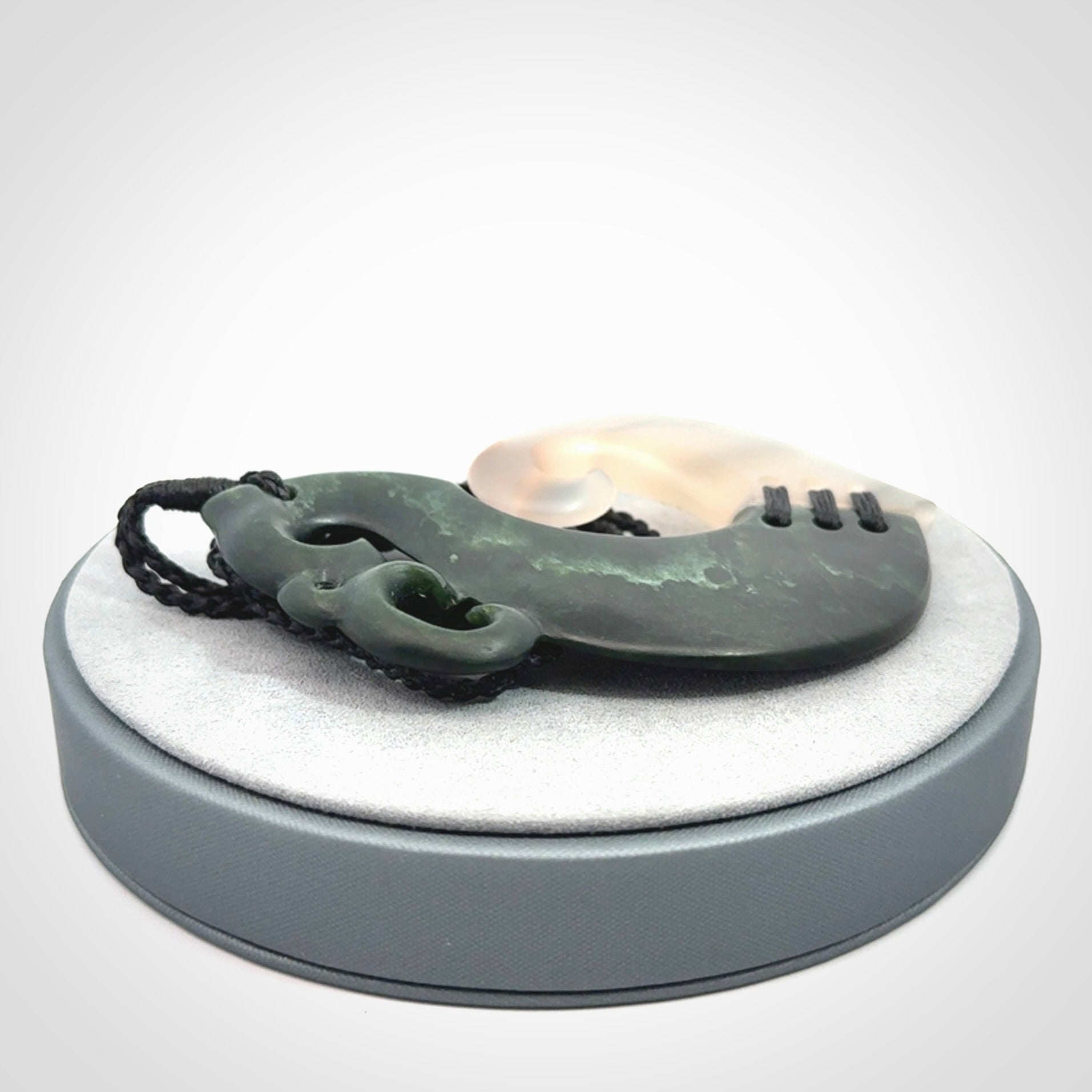 This photo shows a wonderful hand carved New Zealand jade and Japanese Agate Manaia with hook pendant. The hook is suspended on a black four plait cord that is length adjustable.