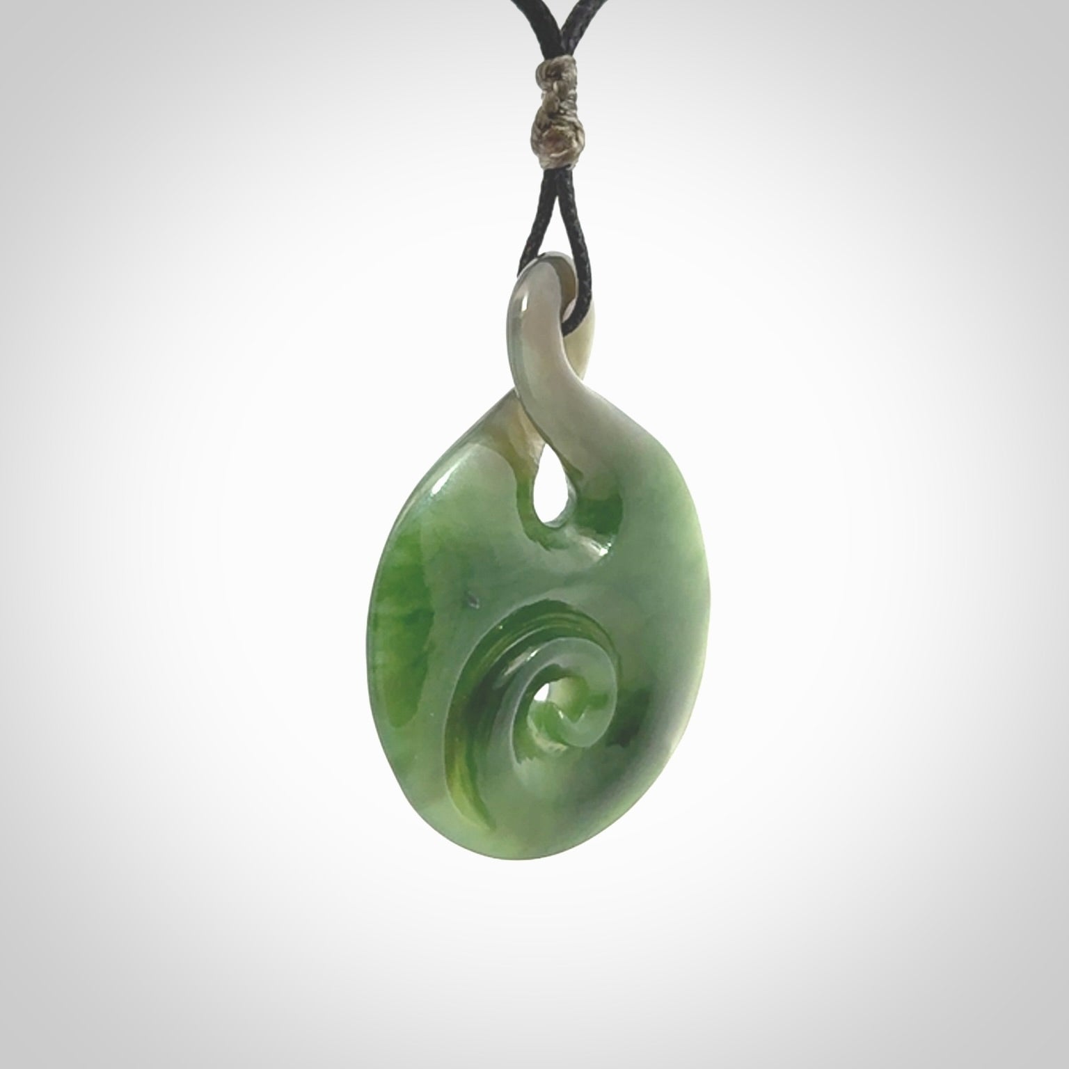 Hand carved New Zealand Jade Twist with Koru heart pendant. Unique Jade jewellery online for sale. Hand made Jade Twist with Koru, provided on adjustable cords and packaged in a woven kete pouch.