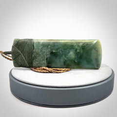 A large and beautiful hand carved toki pendant. This piece is carved from New Zealand jade by NZ Pacific. This is a wonderful large toki bound with a tan cord and a traditional sage green lashing. A beautiful, traditional toki for sale online.