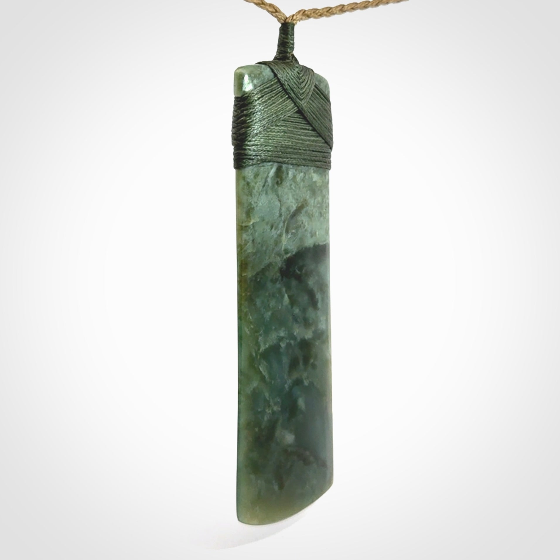 A large and beautiful hand carved toki pendant. This piece is carved from New Zealand jade by NZ Pacific. This is a wonderful large toki bound with a tan cord and a traditional sage green lashing. A beautiful, traditional toki for sale online.