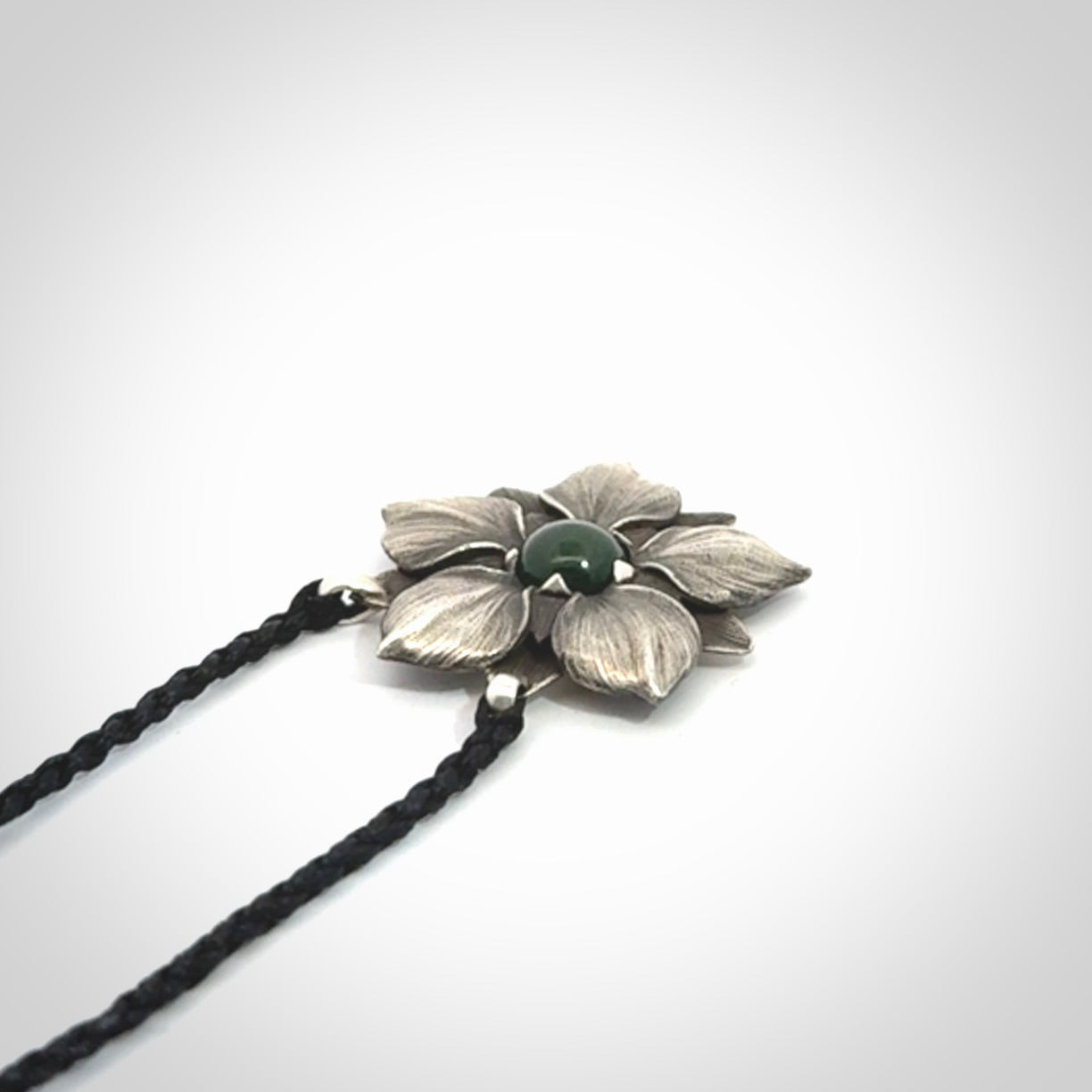 This is a hand carved Sterling Silver Manuka Flower pendant with New Zealand Jade insert. This is a medium sized necklace and is provided with an adjustable black cord.