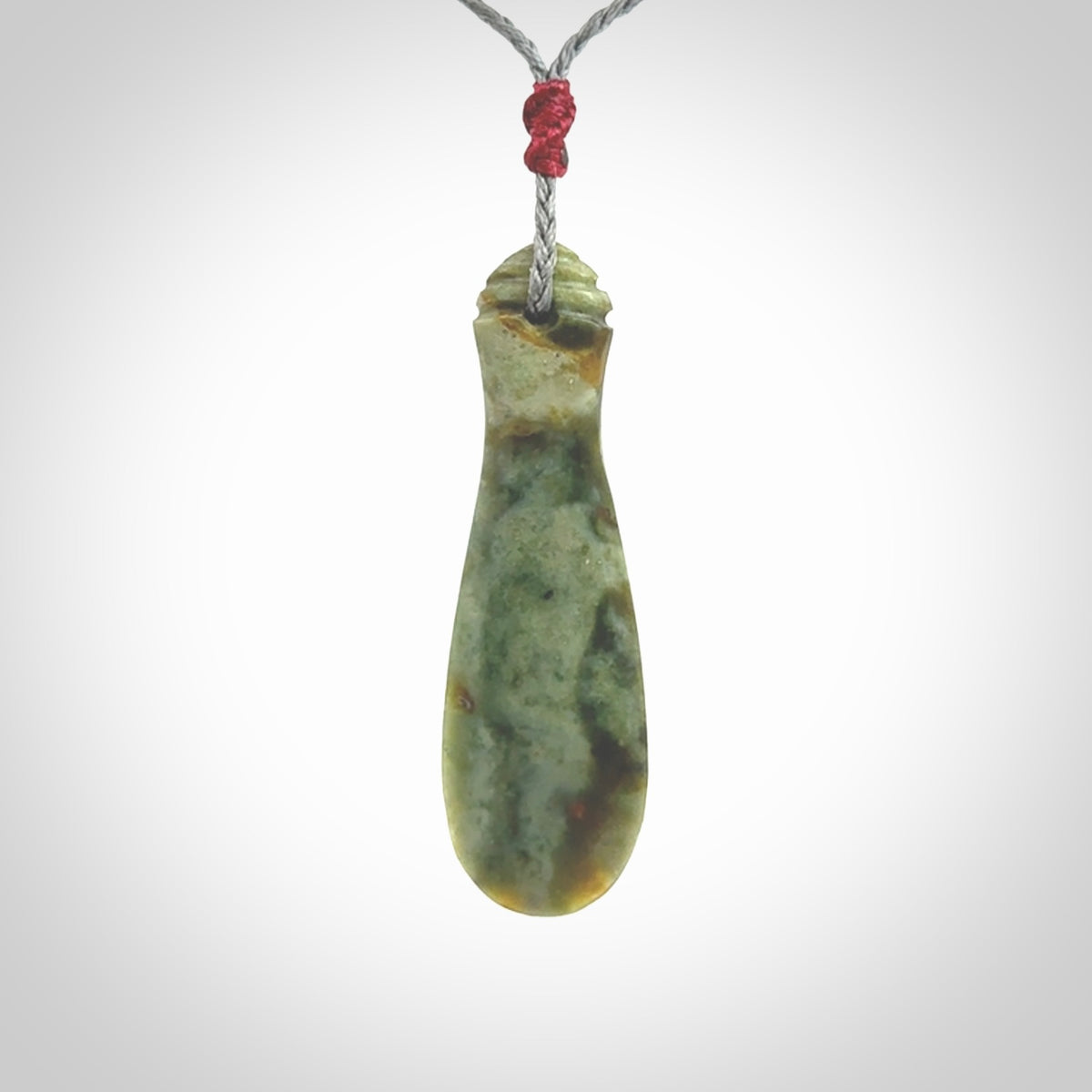 This is a sleek and slender hand carved New Zealand Jade mere pendant. The stone is a very beautiful green and the cord is either black, red or grey and is adjustable. The pendant has a light polish and just glows. Provided in a woven kete pouch.