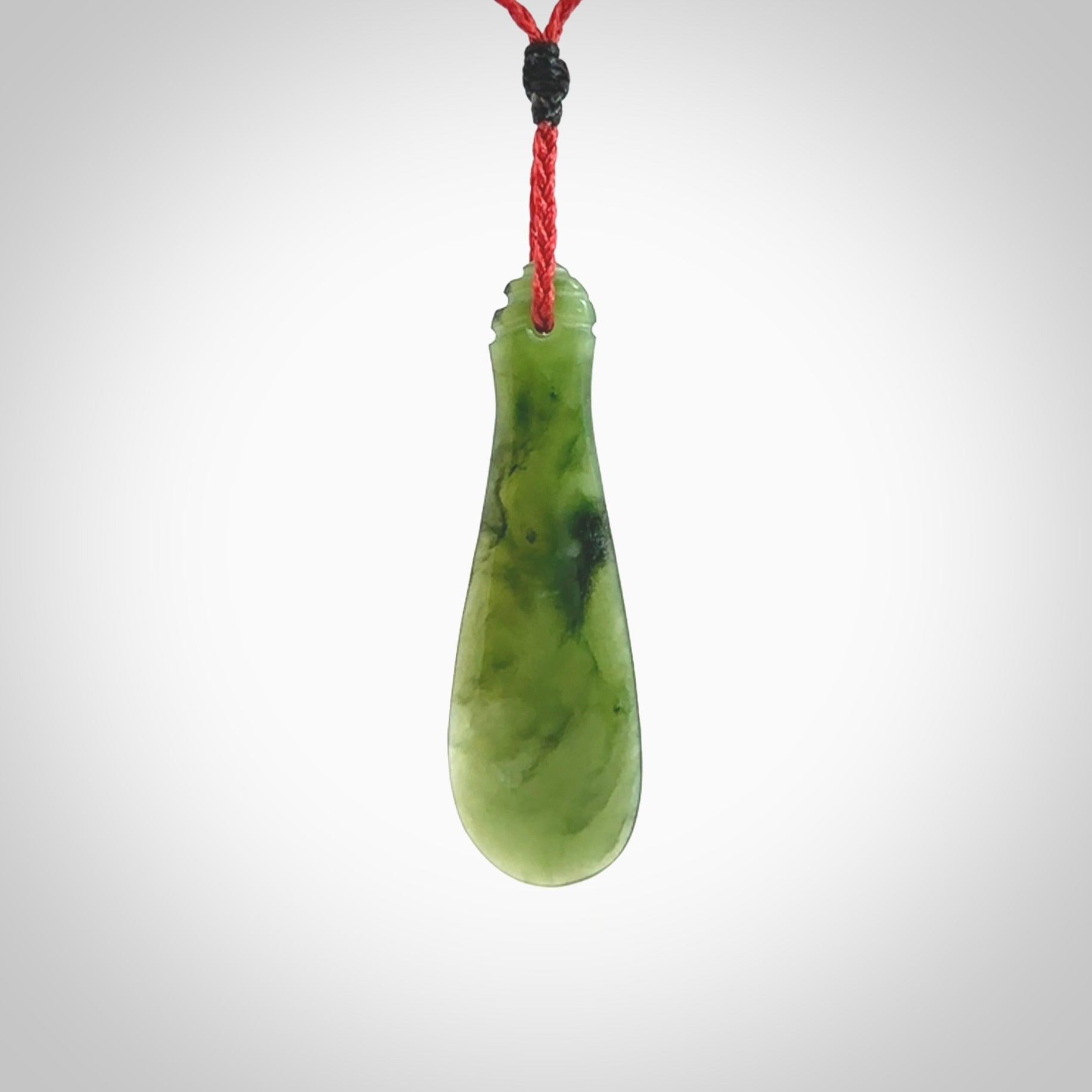 This is a sleek and slender hand carved New Zealand Jade mere pendant. The stone is a very beautiful green and the cord is either black, red or green and is adjustable. The pendant has a light polish and just glows. Provided in a woven kete pouch.