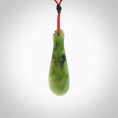 This is a sleek and slender hand carved New Zealand Jade mere pendant. The stone is a very beautiful green and the cord is either black, red or green and is adjustable. The pendant has a light polish and just glows. Provided in a woven kete pouch.