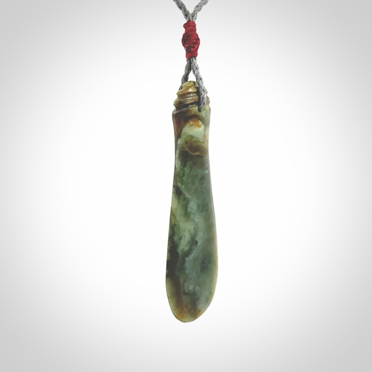This is a sleek and slender hand carved New Zealand Jade mere pendant. The stone is a very beautiful green and the cord is either black, red or grey and is adjustable. The pendant has a light polish and just glows. Provided in a woven kete pouch.