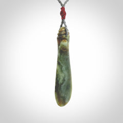 This is a sleek and slender hand carved New Zealand Jade mere pendant. The stone is a very beautiful green and the cord is either black, red or grey and is adjustable. The pendant has a light polish and just glows. Provided in a woven kete pouch.