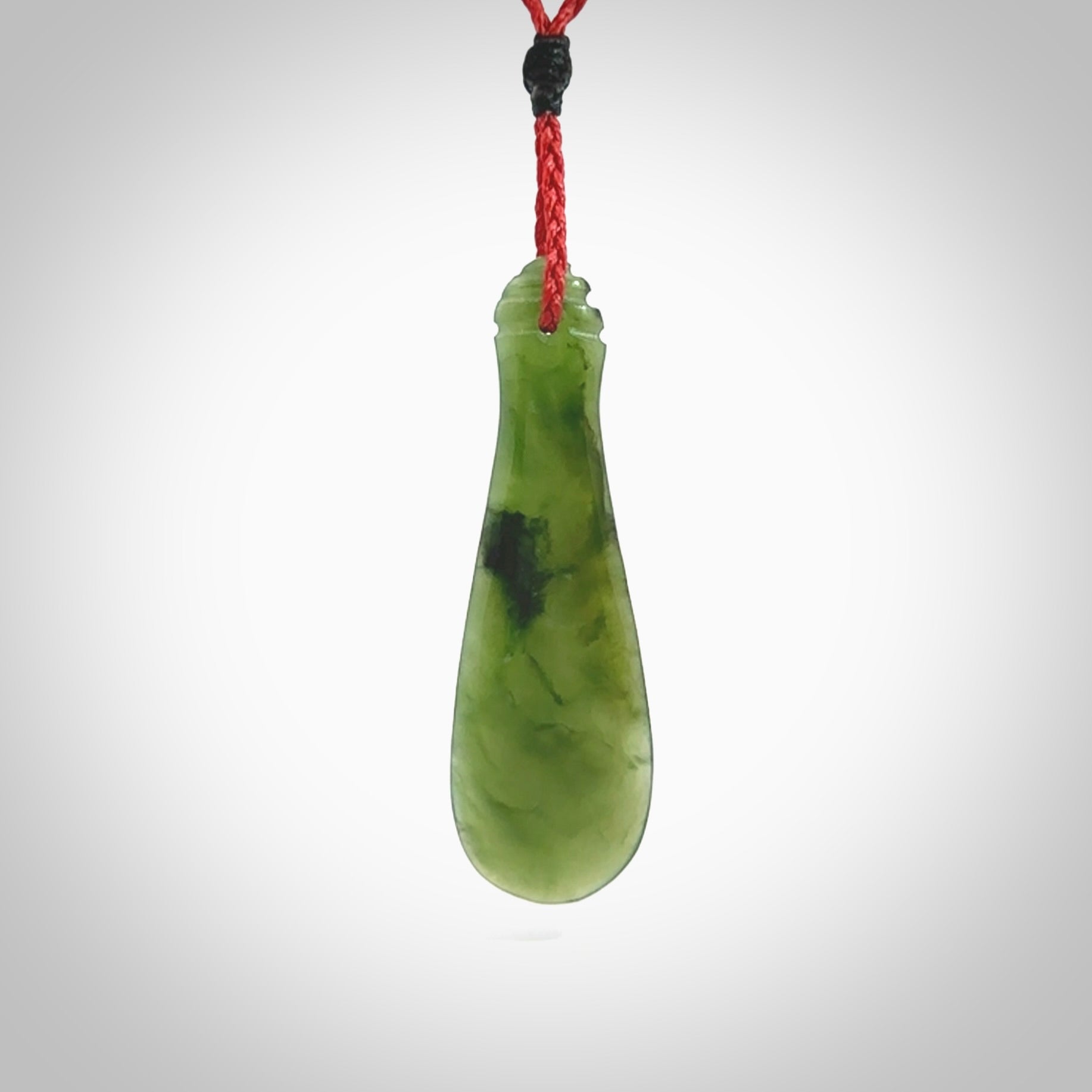 This is a sleek and slender hand carved New Zealand Jade mere pendant. The stone is a very beautiful green and the cord is either black, red or green and is adjustable. The pendant has a light polish and just glows. Provided in a woven kete pouch.