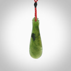 This is a sleek and slender hand carved New Zealand Jade mere pendant. The stone is a very beautiful green and the cord is either black, red or green and is adjustable. The pendant has a light polish and just glows. Provided in a woven kete pouch.
