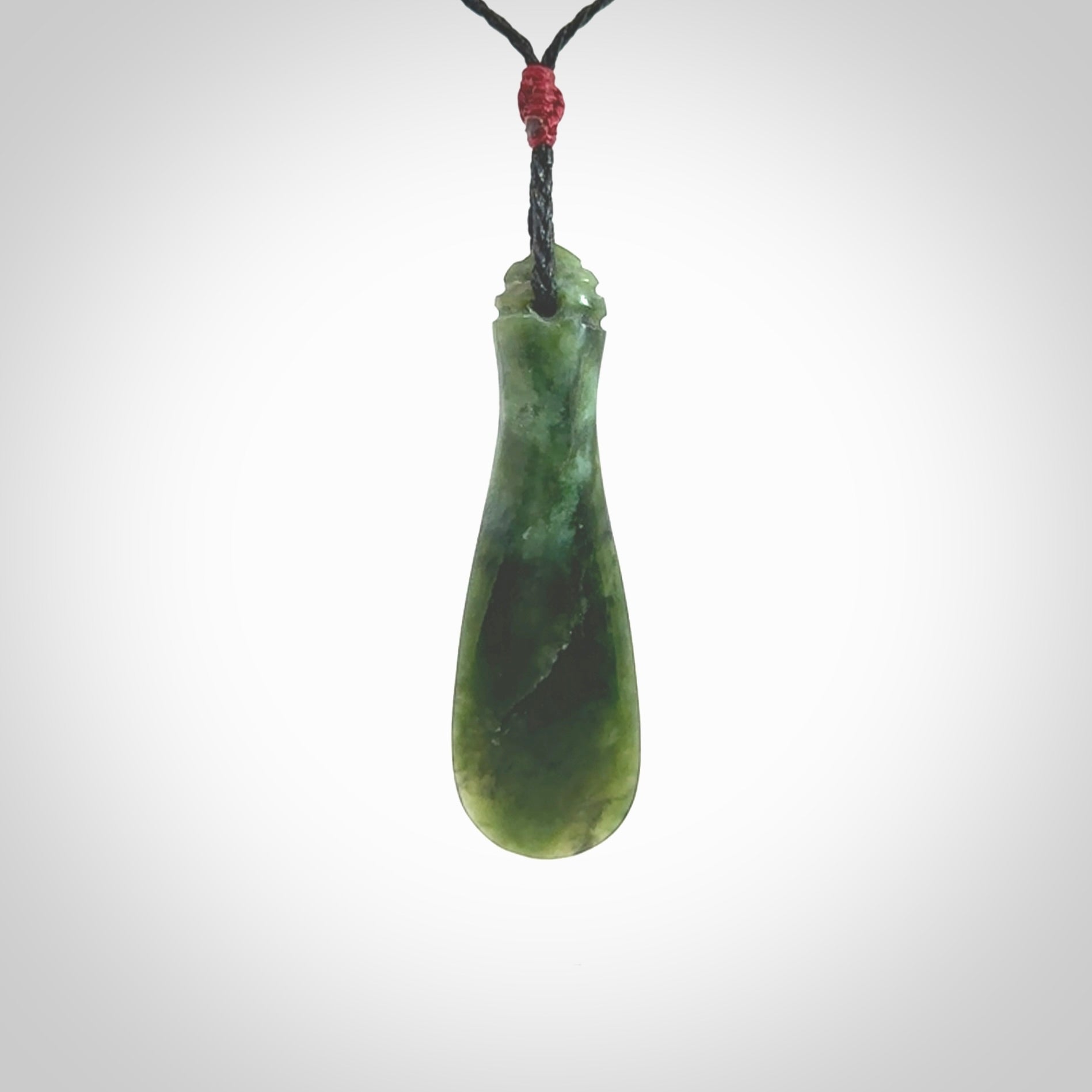 This is a sleek and slender hand carved New Zealand Jade mere pendant. The stone is a very beautiful green and the cord is either black, red or green and is adjustable. The pendant has a light polish and just glows. Provided in a woven kete pouch.