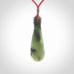 This is a sleek and slender hand carved New Zealand Jade mere pendant. The stone is a very beautiful green and the cord is either black, red or grey and is adjustable. The pendant has a light polish and just glows. Provided in a woven kete pouch.