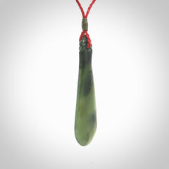 This is a sleek and slender hand carved New Zealand Jade mere pendant. The stone is a very beautiful green and the cord is either black, red or grey and is adjustable. The pendant has a light polish and just glows. Provided in a woven kete pouch.