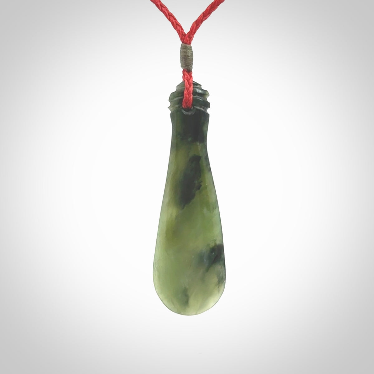 This is a sleek and slender hand carved New Zealand Jade mere pendant. The stone is a very beautiful green and the cord is either black, red or grey and is adjustable. The pendant has a light polish and just glows. Provided in a woven kete pouch.