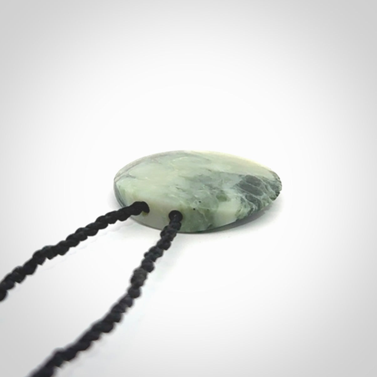 This piece is a small oval round, disc pendant hand carved in New Zealand jade.