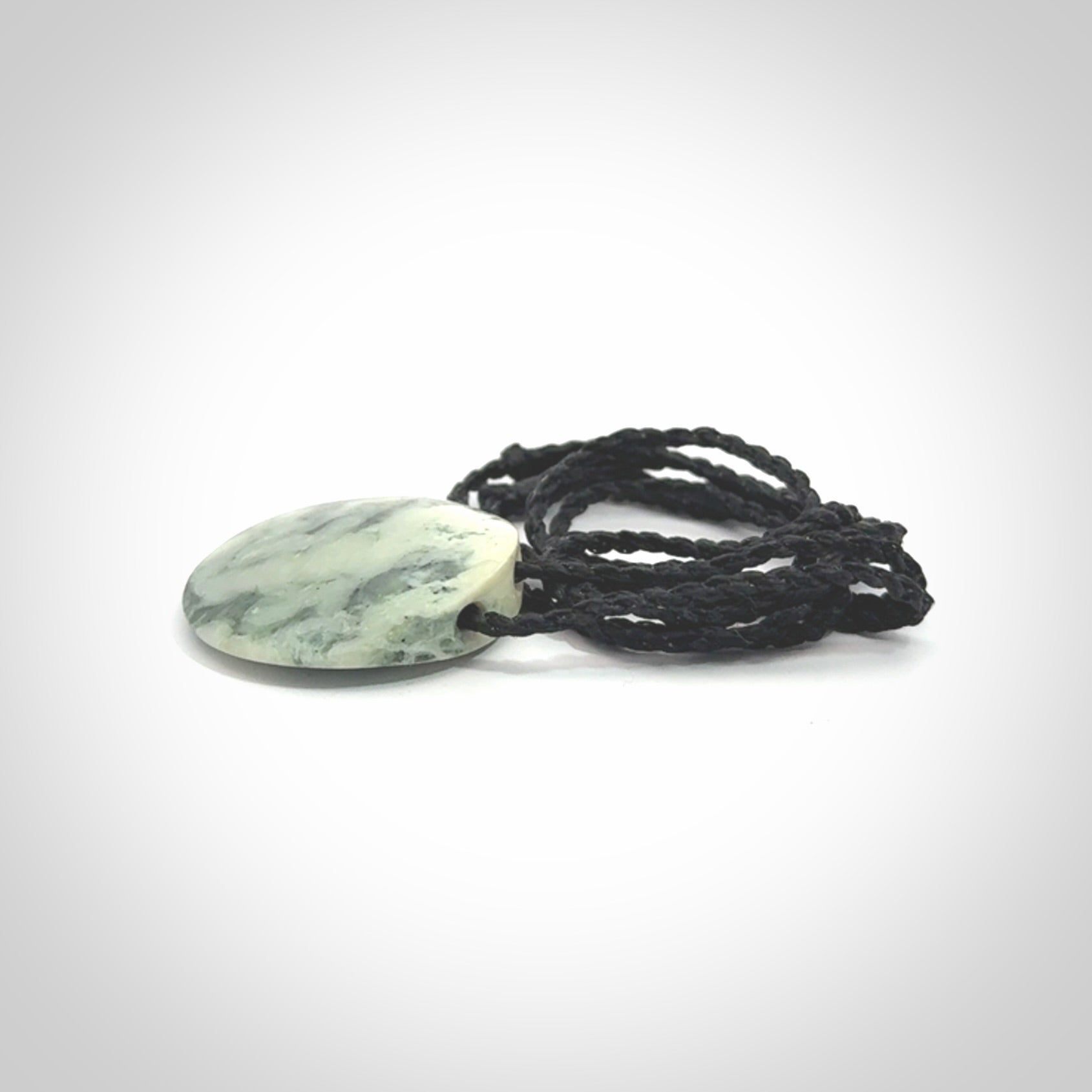 This piece is a small oval round, disc pendant hand carved in New Zealand jade.