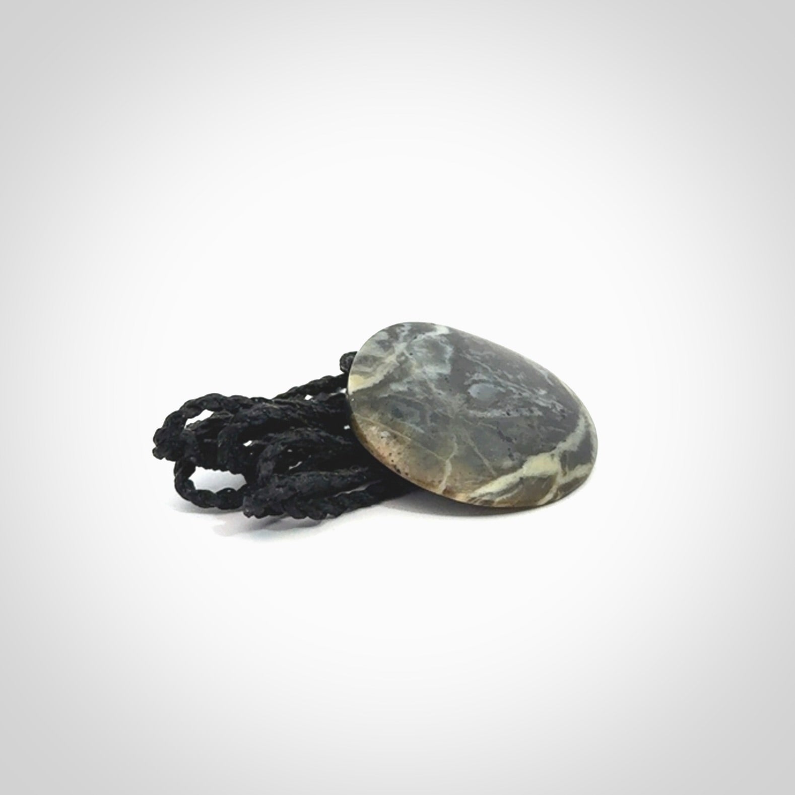 This piece is a small oval round, disc pendant hand carved in New Zealand jade.