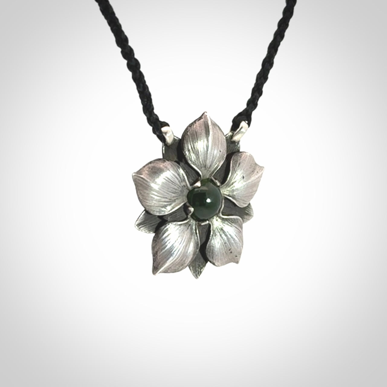 This is a hand carved Sterling Silver Manuka Flower pendant with New Zealand Jade insert. This is a medium sized necklace and is provided with an adjustable black cord.